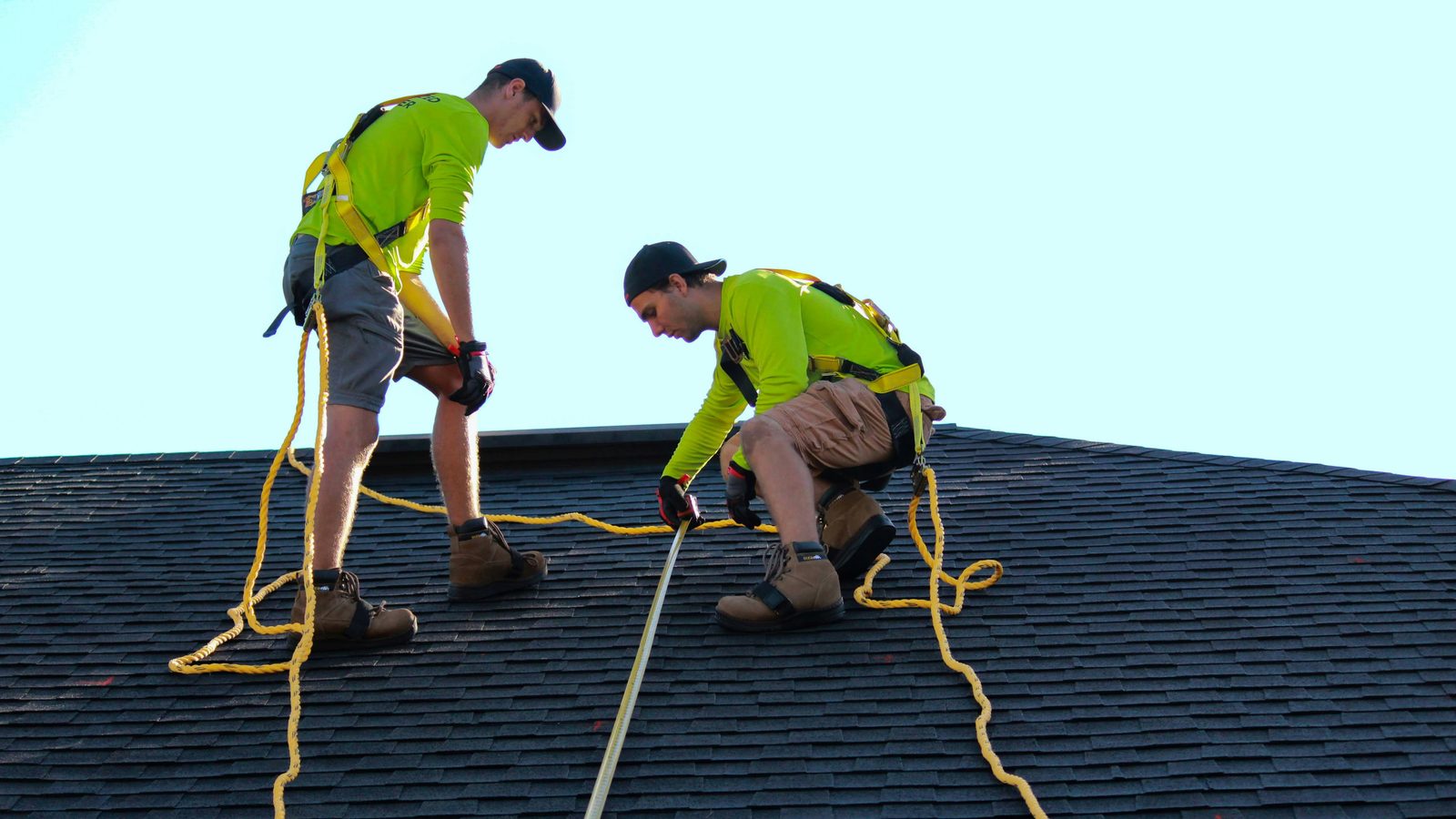 Roofers working on a dark shingle roof