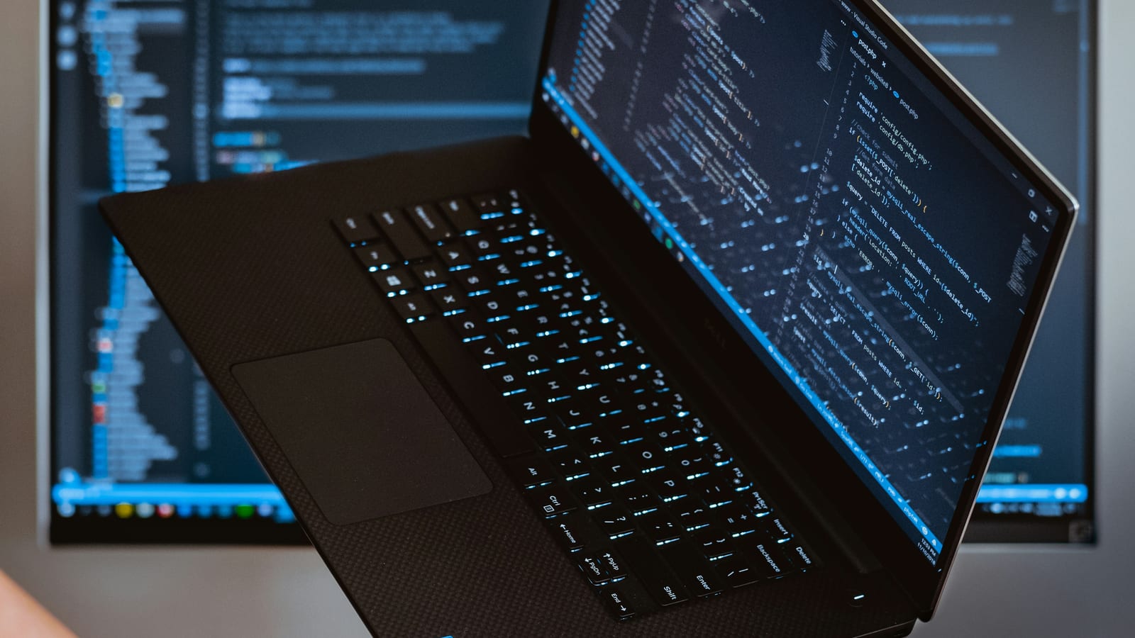 A backlit laptop showing code on a dark desk, with a second screen behind